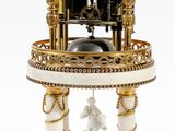 une horloge dorée et blanche posée sur un socle, sur une surface blanche