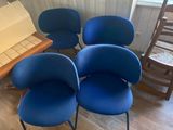 quatre chaises bleues placées dans une pièce, à côté d'une table en bois