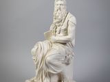 une statue blanche représentant un homme assis sur une chaise, un livre à la main