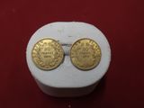 two gold coins sitting on top of a white box