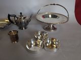 silver dishes and cups on a table next to a red vase