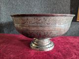 a silver bowl on a red cloth with a painting in the background