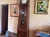 une horloge de parquet au milieu d'une pièce, avec des tableaux accrochés aux murs