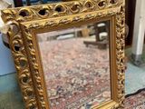 a gold framed mirror sitting on top of a rug next to a chair