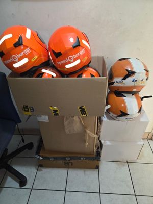 Plusieurs casques orange se trouvent dans une boîte en carton posée sur un sol carrelé.