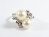 une photo d'une bague en perle blanche et diamants posée sur une surface blanche