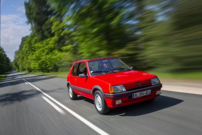 a red car driving down the road with trees in the background