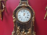 une horloge dorée posée sur une table en verre devant un mur rouge