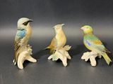 three small figurines of birds sitting on a tree branch