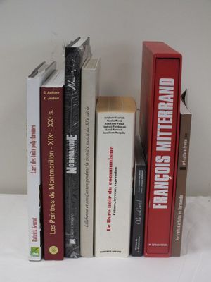 Plusieurs livres sont alignés sur une table blanche, avec une horloge en arrière-plan.