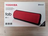 La boîte est ouverte sur une table sur laquelle se trouve un haut-parleur rouge.