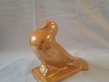 une statue d'oiseau dorée posée sur un socle, sur fond blanc