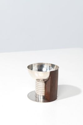 un petit bol en métal reposant sur un socle en bois, posé sur une surface blanche