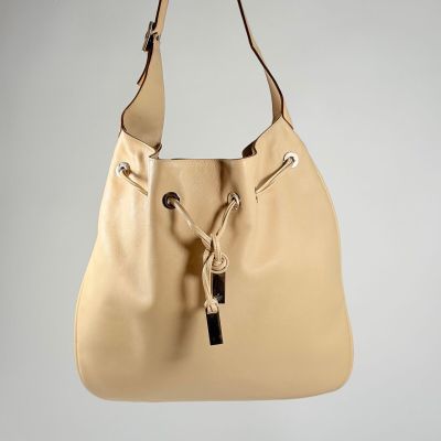 Le grand sac beige est accroché à un crochet fixé au mur.