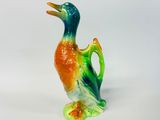 un petit canard en céramique posé sur une surface blanche