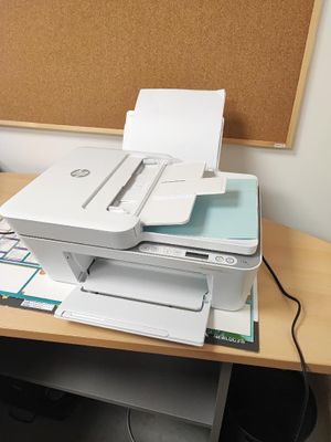 une imprimante posée sur un bureau, devant un tableau en liège