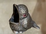 figurine en argent représentant un oiseau aux yeux rouges, posé sur une table en verre