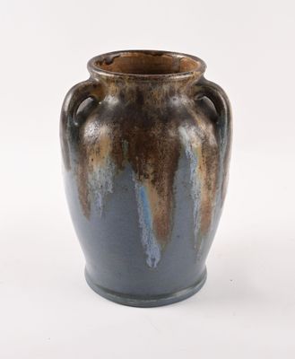 un vase brun et bleu posé sur une surface blanche