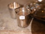 une tasse en argent posée sur une table, à côté d'un plateau sur lequel se trouvent d'autres tasses en argent