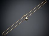 a gold necklace with a pearl on a black background