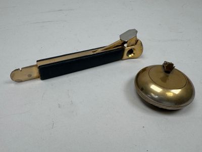 une cloche en laiton et une poignée noire posées sur une table blanche
