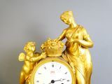 une horloge en or surmontée d'une statue représentant une femme tenant un panier de fleurs