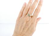 a woman ' s hand holding a ring with a green stone