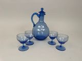 un pichet en verre bleu et quatre verres sur une table