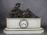 une statue représentant une femme assise sur un socle de marbre, avec une horloge devant elle