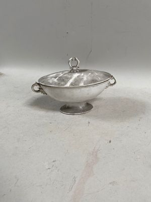 un bol en argent muni d'une anse, posé sur une table blanche