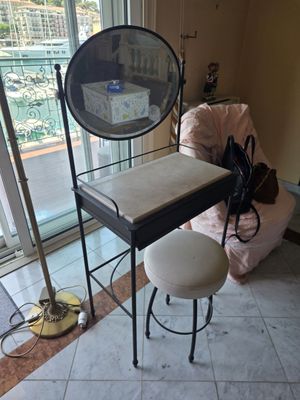 a small table with a mirror and stool in front of a window