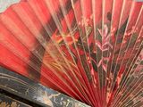 someone is holding a red and black fan with gold designs on it