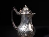 an antique silver coffee pot on a stand against a black background