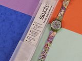 une montre posée sur une surface colorée, à côté d'un stylo