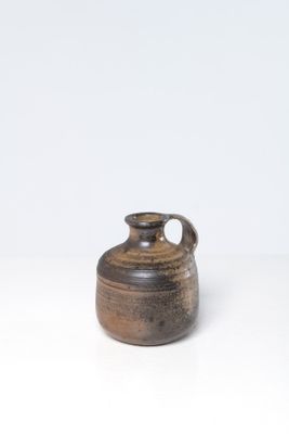 un petit vase brun posé sur une surface blanche