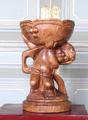 une statue en bois représentant un homme tenant un bol sur la tête