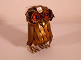 a metal owl with red eyes sitting on a white surface