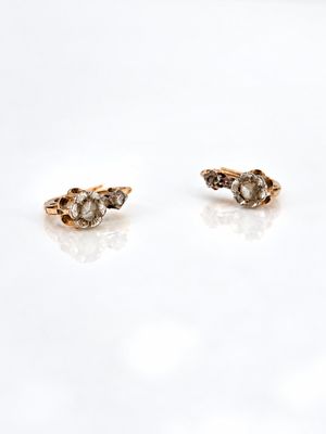 a pair of gold and diamond earrings sitting on top of a white surface