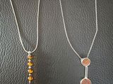 two necklaces on a black leather surface with a silver chain