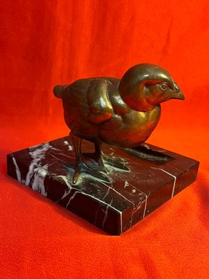 sculpture en bronze représentant un oiseau, posée sur un socle en marbre, sur fond rouge