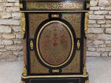 a black and gold painted cabinet sitting in front of a brick wall