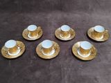 six cups and saucers with gold designs on them on a table