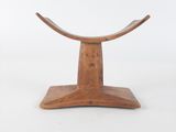 un petit tabouret en bois avec une assise incurvée posée sur une surface blanche