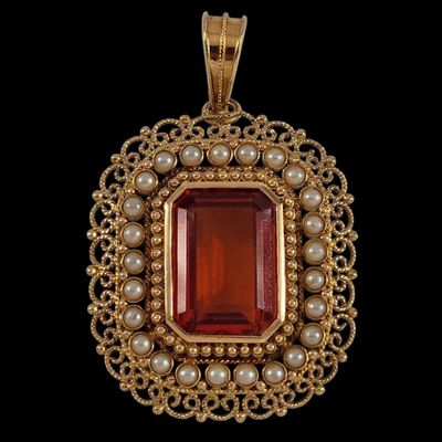 un pendentif en or orné d'une pierre rouge entourée de perles