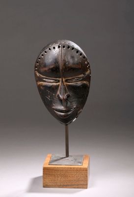 un gros plan d'un masque posé sur un socle en bois, sur fond gris