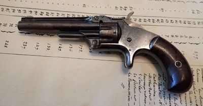 un vieux revolver posé sur une feuille de papier, sur une table