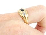 a man ' s hand holding a gold ring with a black and white diamond
