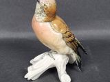 porcelain figurine of a bird sitting on a branch on a gray background