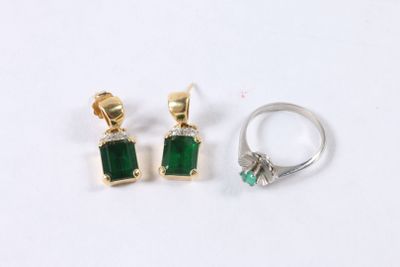 deux boucles d'oreilles en émeraude et diamant et une bague posées sur un fond blanc