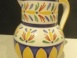a colorful pitcher sitting on a table with a black wall in the background